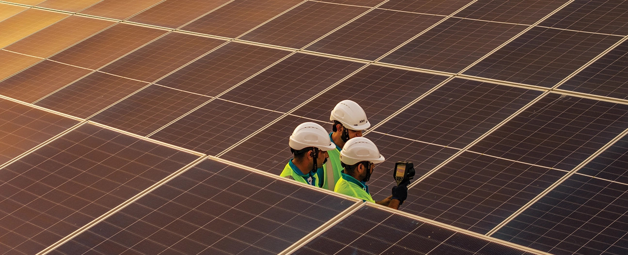 Engineers with thermal camera inspecting solar panels at sunset